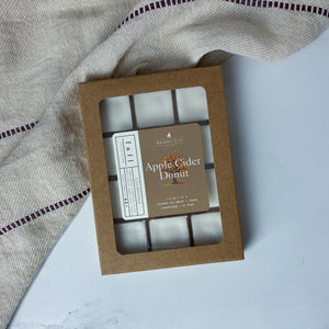 Box of Apple Cider Donut wax melts on a marble surface with a striped fabric background