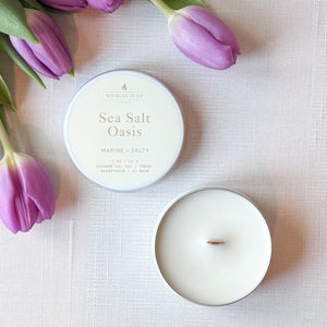 Candle labeled 'Sea Salt Oasis' with a bouquet of purple tulips on a light fabric background