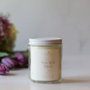 Candle jar labeled 'Sea Salt Oasis' with flowers in the background