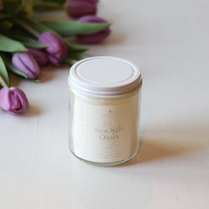 Jar of 'Sea Salt Oasis' candle with purple tulips on a white surface