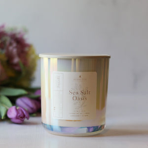 Candle labeled 'Sea Salt Oasis' with a bouquet of flowers in the background
