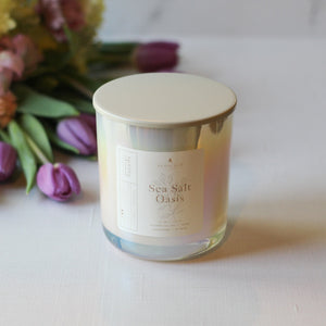 Candle labeled 'Sea Salt Oasis' with flowers in the background on a light surface