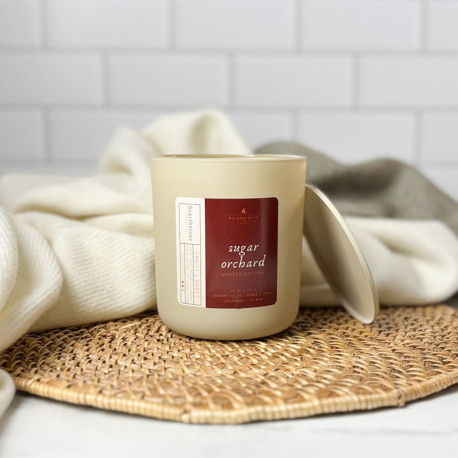 Candle labeled 'Sugar Orchard' on a woven mat with a white towel in the background