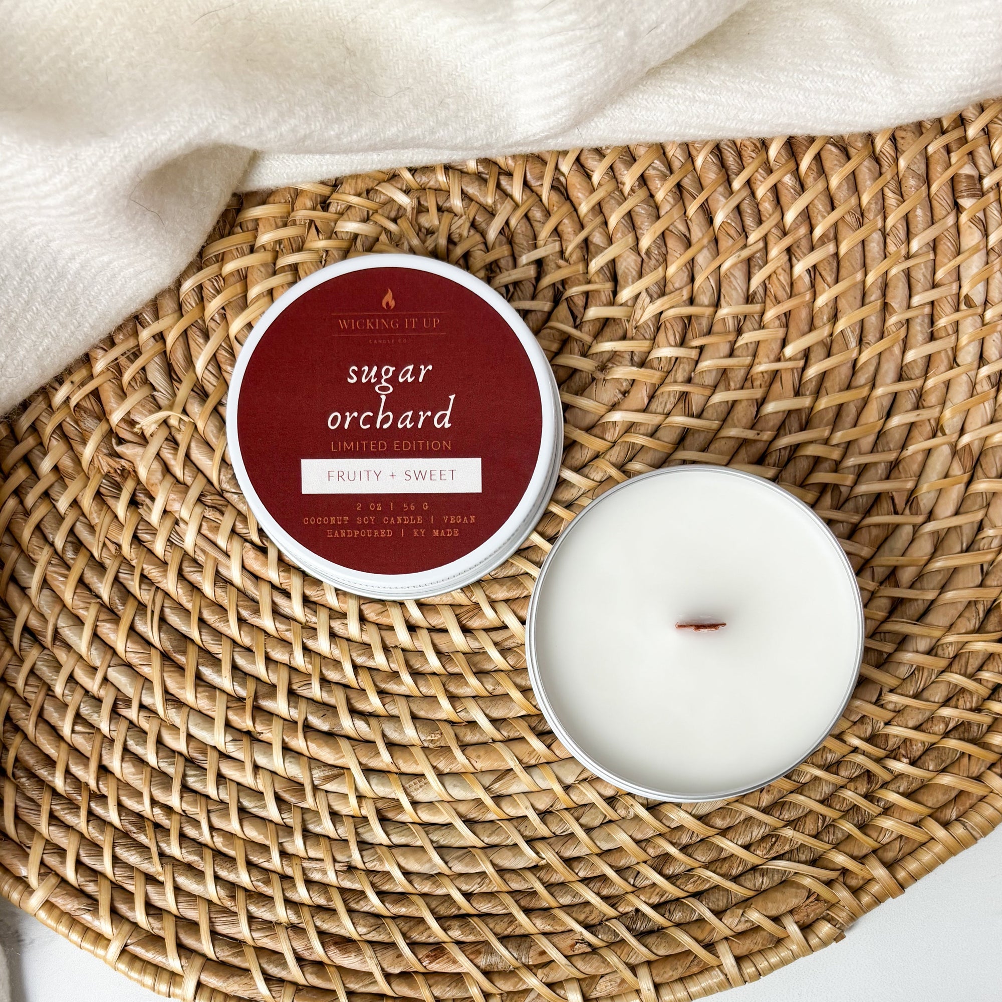 Candle and packaging labeled 'Sugar Orchard' on a woven mat.