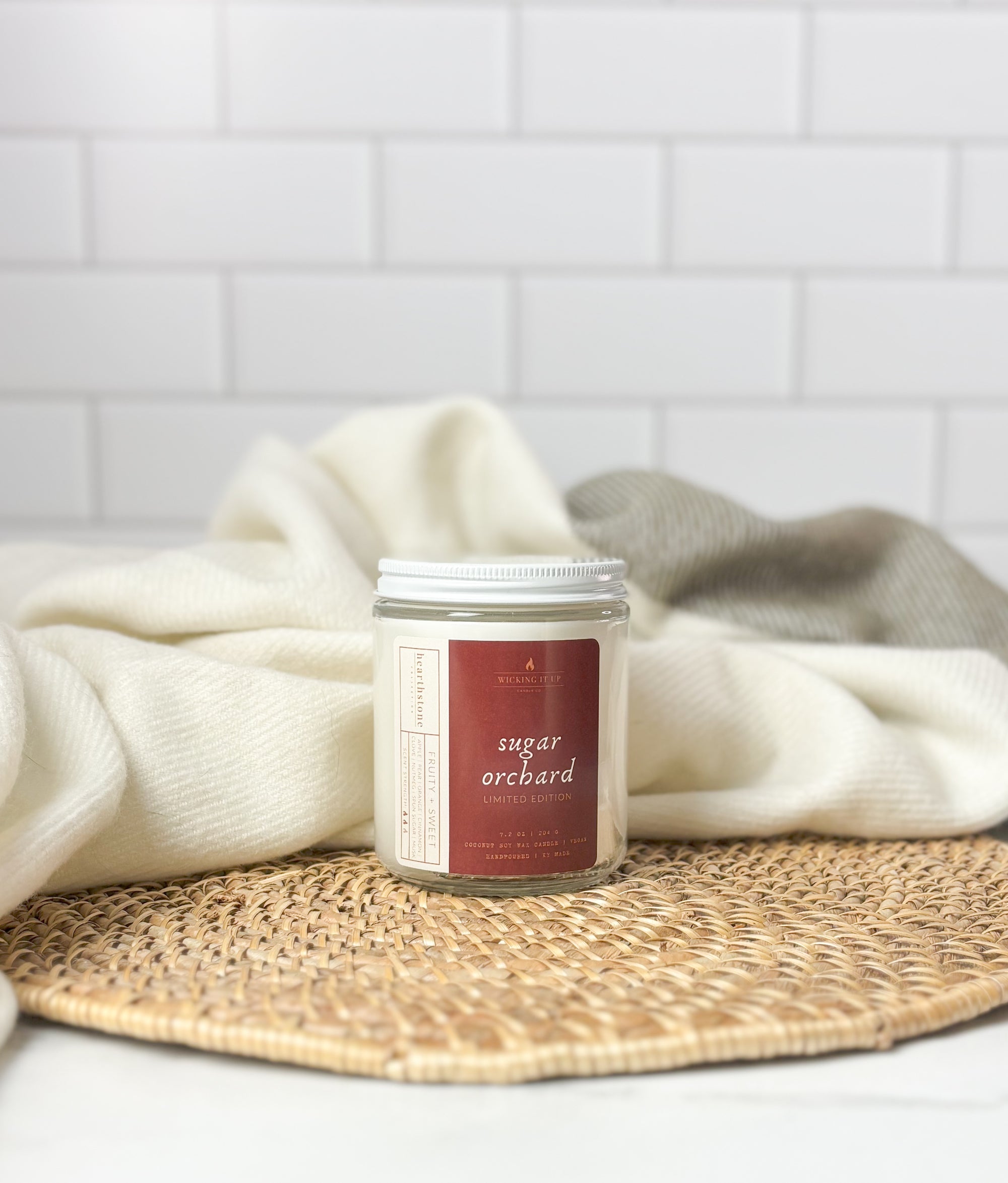 Candle jar labeled 'sugar orchard' on a woven mat with a white towel in the background.