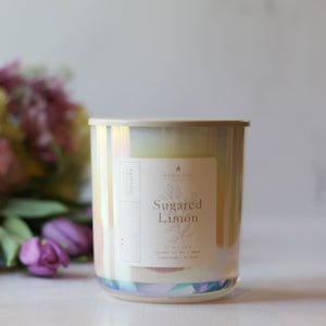 Candle with 'Sugared Limon' label in front of flowers on a light background