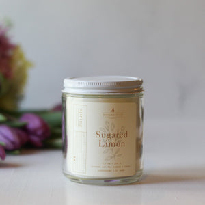 Jar of 'Sugared Limon' candle with flowers in the background