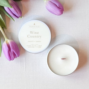 Candle labeled 'Wine Country' with a container and purple tulips on a light background