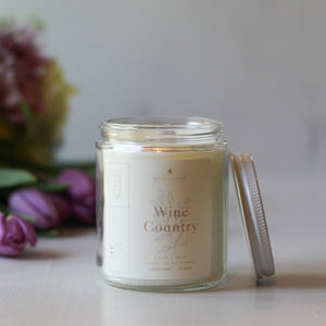 Glass candle jar labeled 'Wine Country' with a blurred floral background